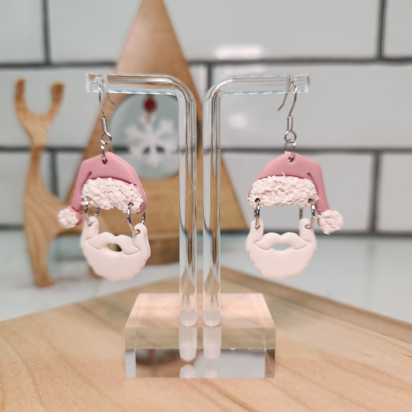 Pair of Santa Claus Earrings with pink and white design on a clear stand against a blurred background