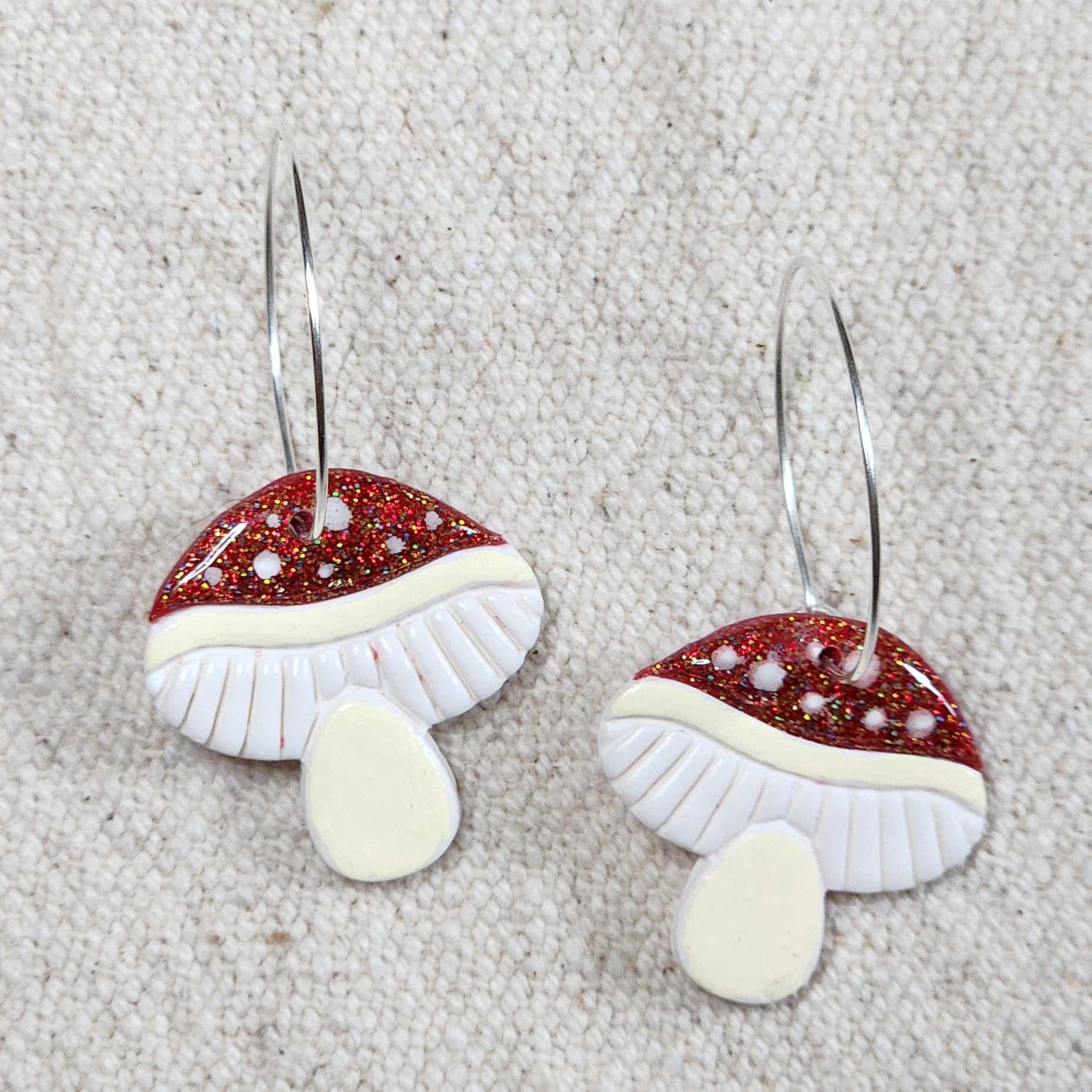 Mushroom earrings on hoops. Caps are glittery red with white polka dots.