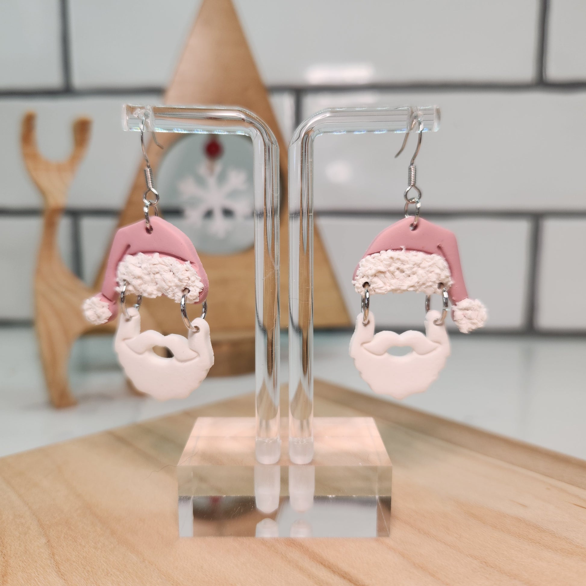 Pair of Santa Claus Earrings with pink and white design on a clear stand against a blurred background